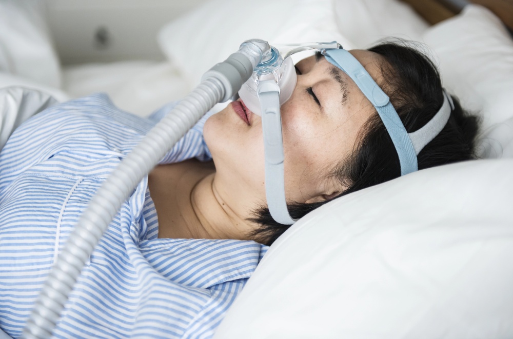 A person in bed wears a striped shirt and CPAP mask, common for OSA or sleep apnoea care in Frenchs Forest.