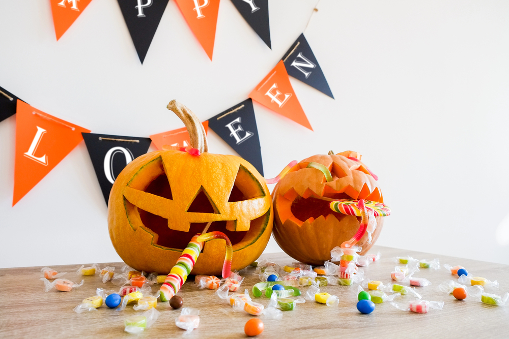 Two carved Halloween pumpkins with colourful lollies spilling from their mouths onto a table.