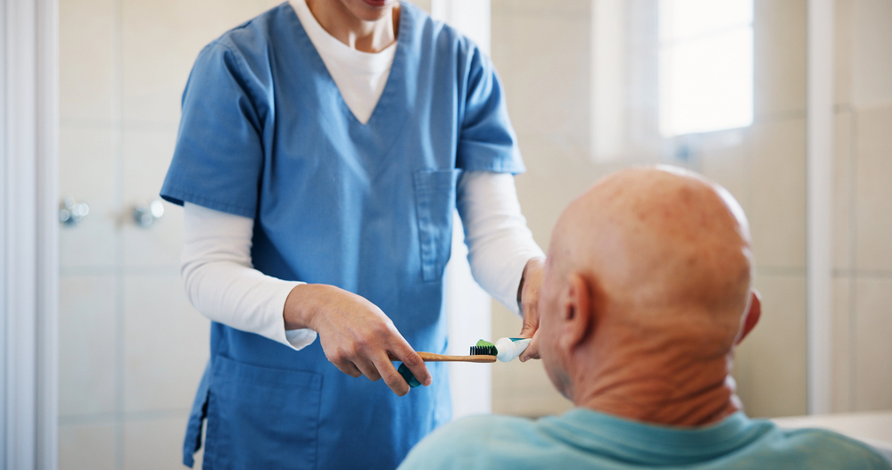 Dental professional assisting an older patient with oral care during a home visit.