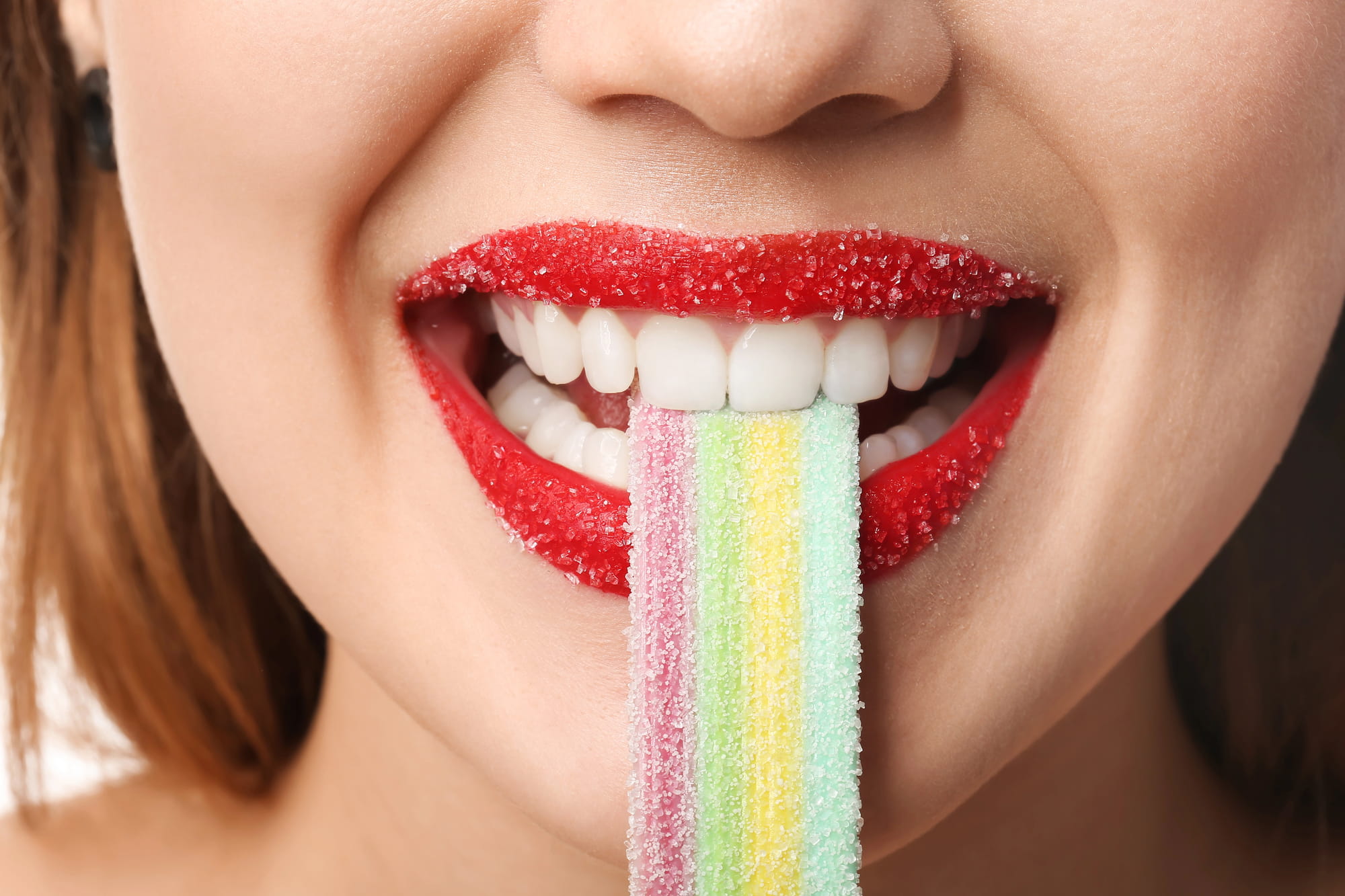 Close-up of a woman biting a rainbow sugar-coated lolly.