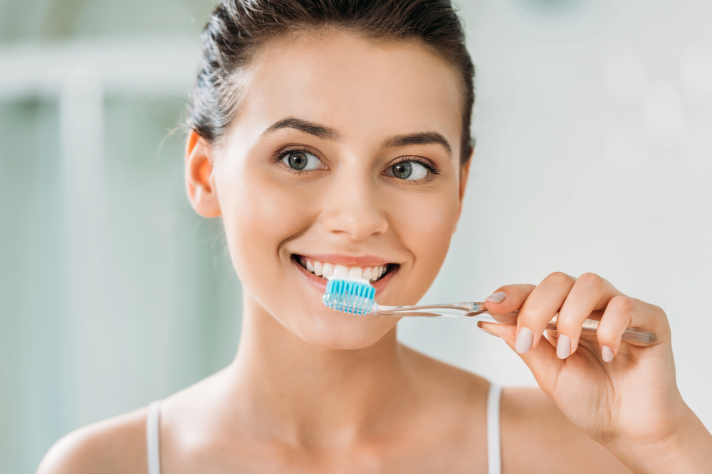 Woman brushing her teeth as part of a twice-daily oral hygiene routine to help remove plaque and maintain healthy teeth and gums.