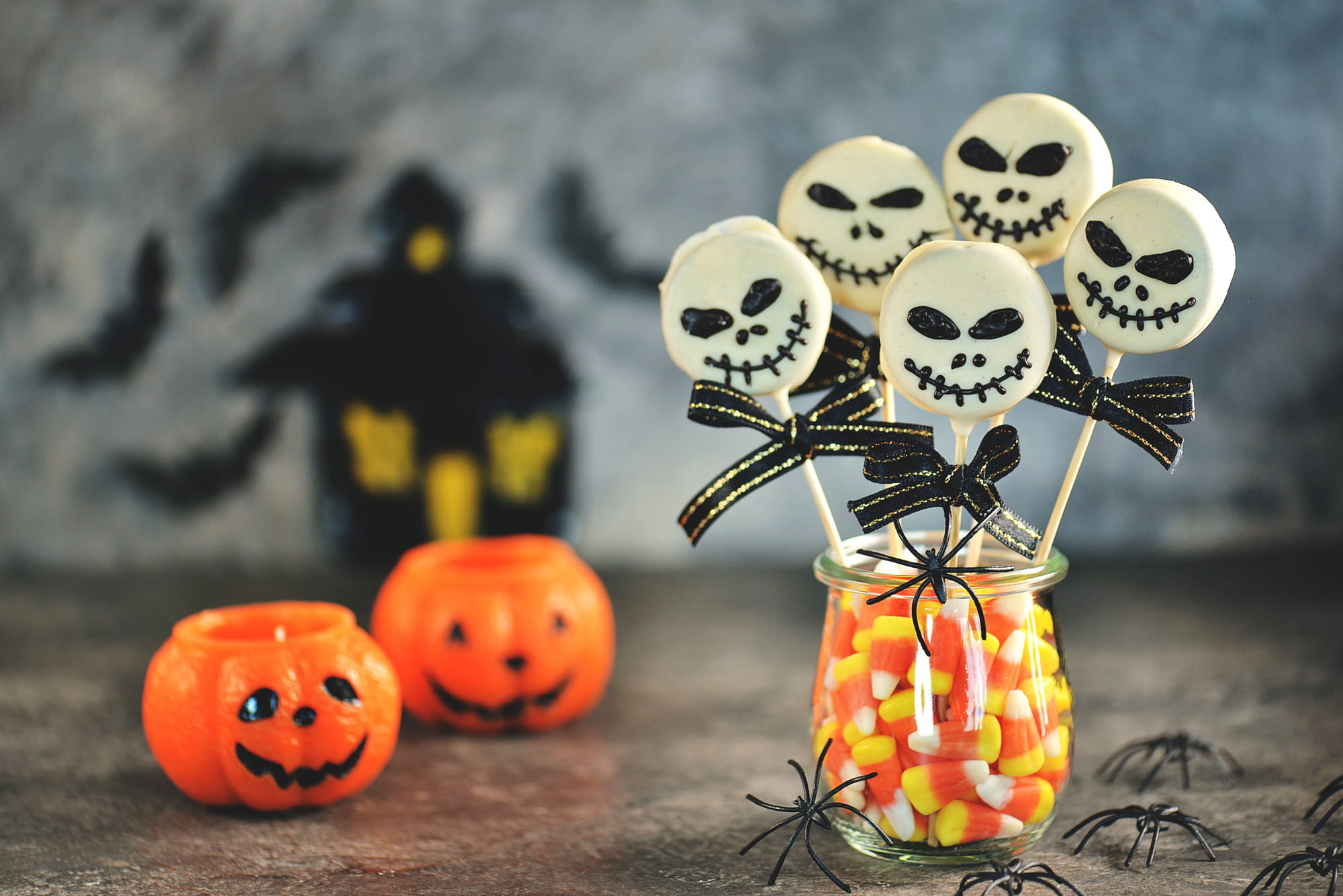 Halloween skull-shaped treats in a jar of candy corn beside pumpkin decorations.