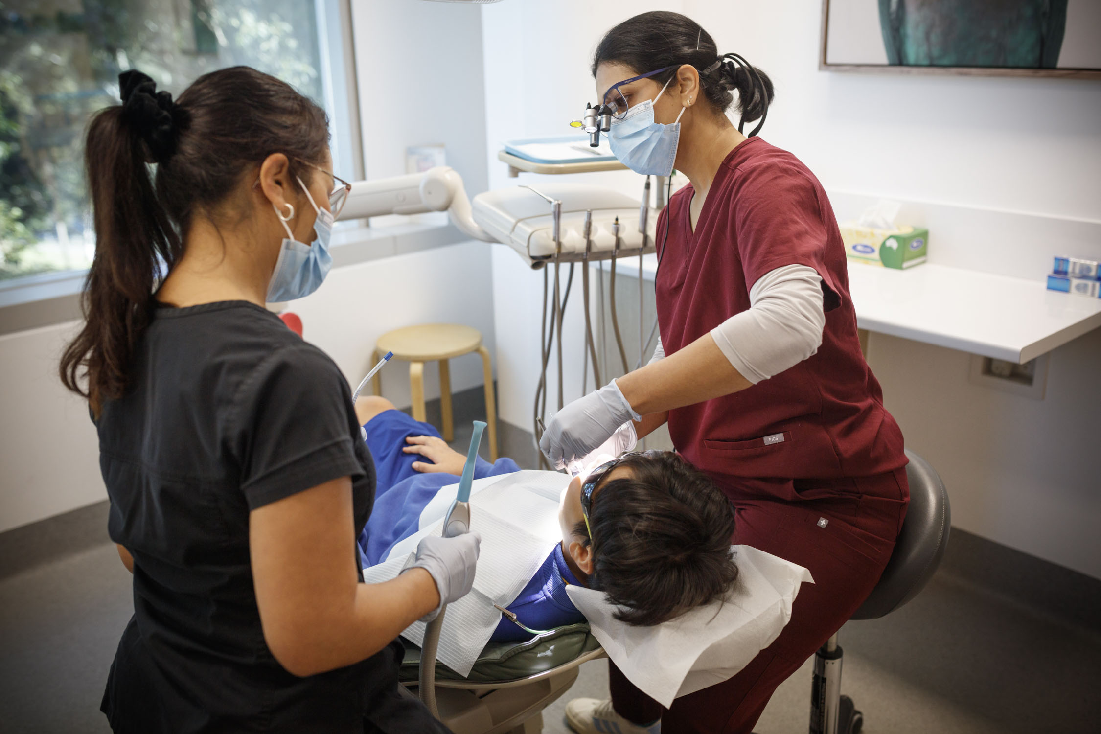 Dentist and assistant use a Tooth Sparkler to treat a child patient; all wear masks and gloves in the clinic.