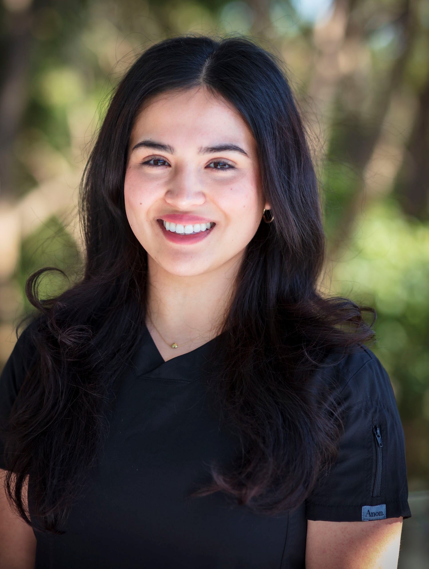 Darlene Barwise smiles outdoors in a black top, with long dark hair and trees blurred behind her.