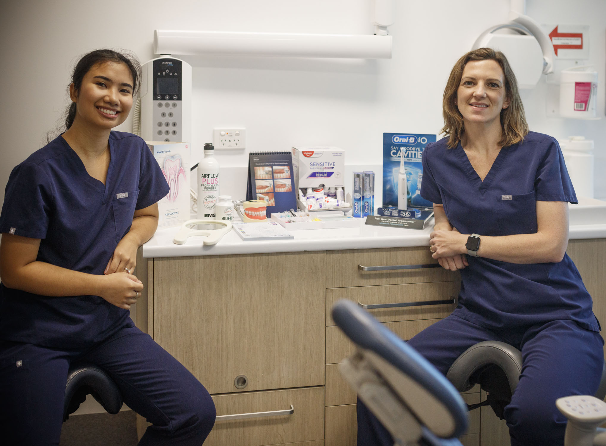 Tooth Sparkler Team women in navy scrubs smile in a dental clinic, surrounded by dental care products.