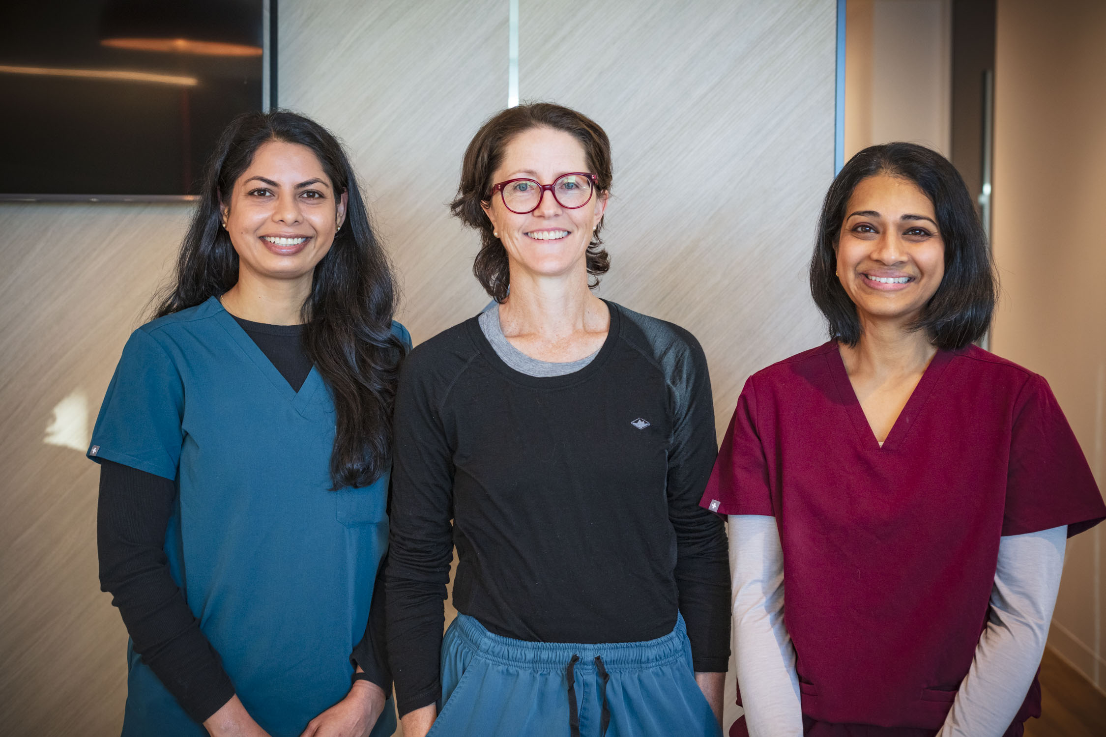 Three women from the Tooth Sparkler Team in scrubs, standing together indoors and smiling at the camera