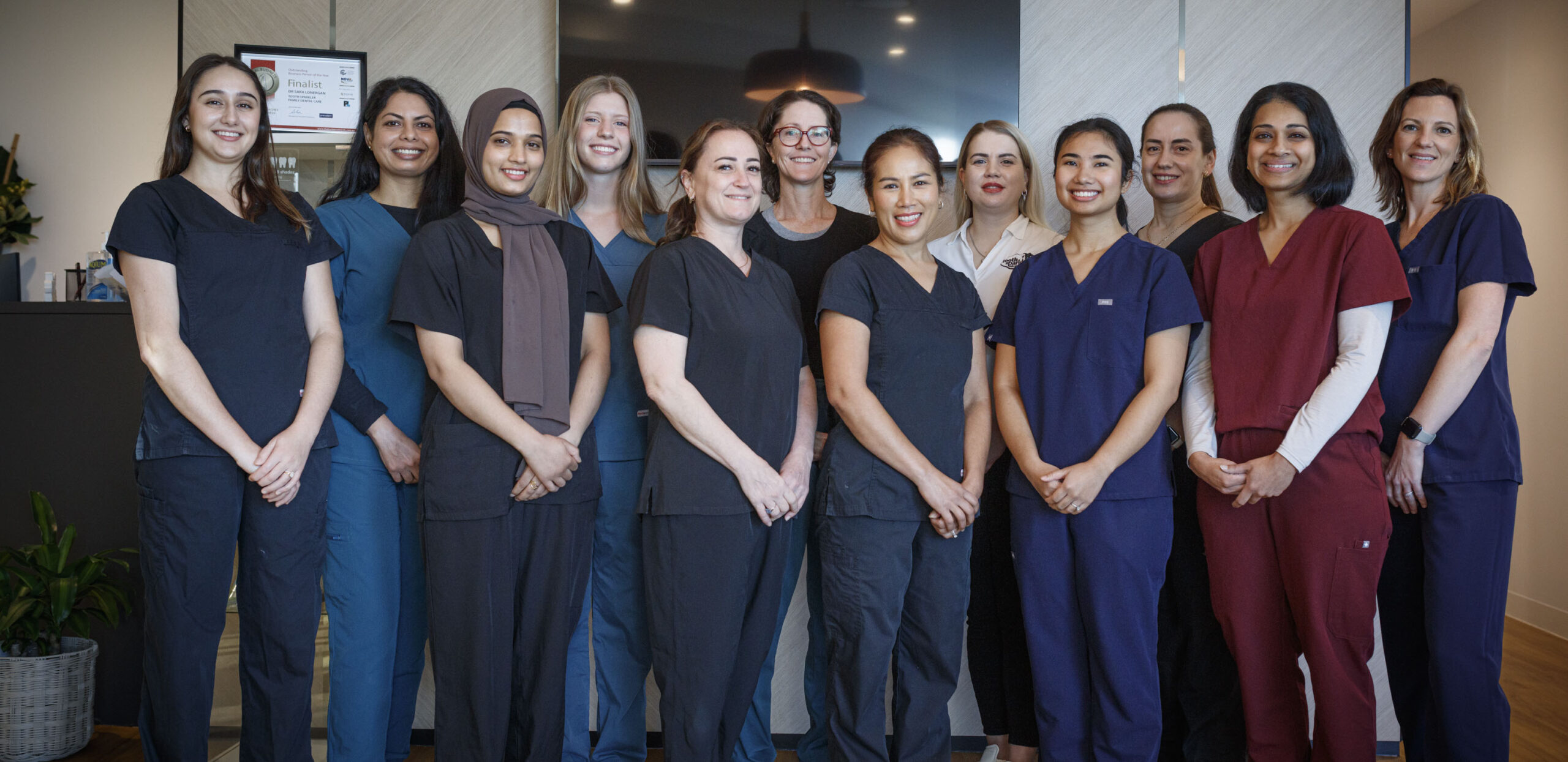 Twelve Toothsparkler Team healthcare professionals wear colorful scrubs and smile in their clinic’s reception area.